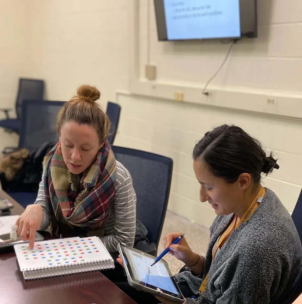 Two school psychologists reviewing student screening data on paper and a tablet