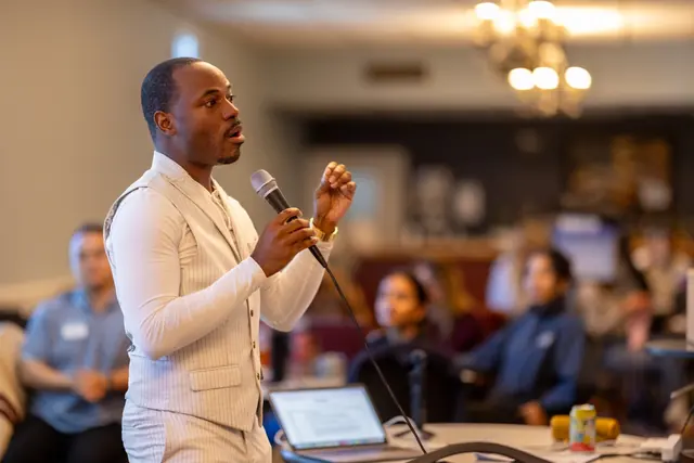 Dr. Byron McClure mid-sentence with a microphone, gesturing to school psychologists seated around him