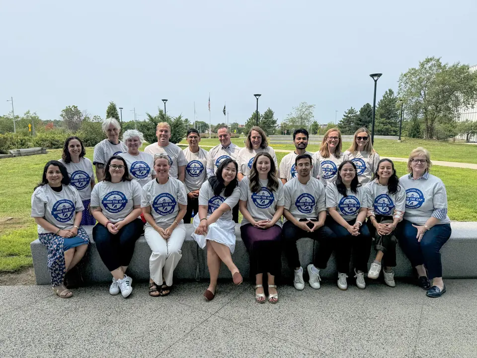 The BHS Research Team, about twenty people in matching Mind the Gap T-shirts, seated and standing outdoors on a sunny day