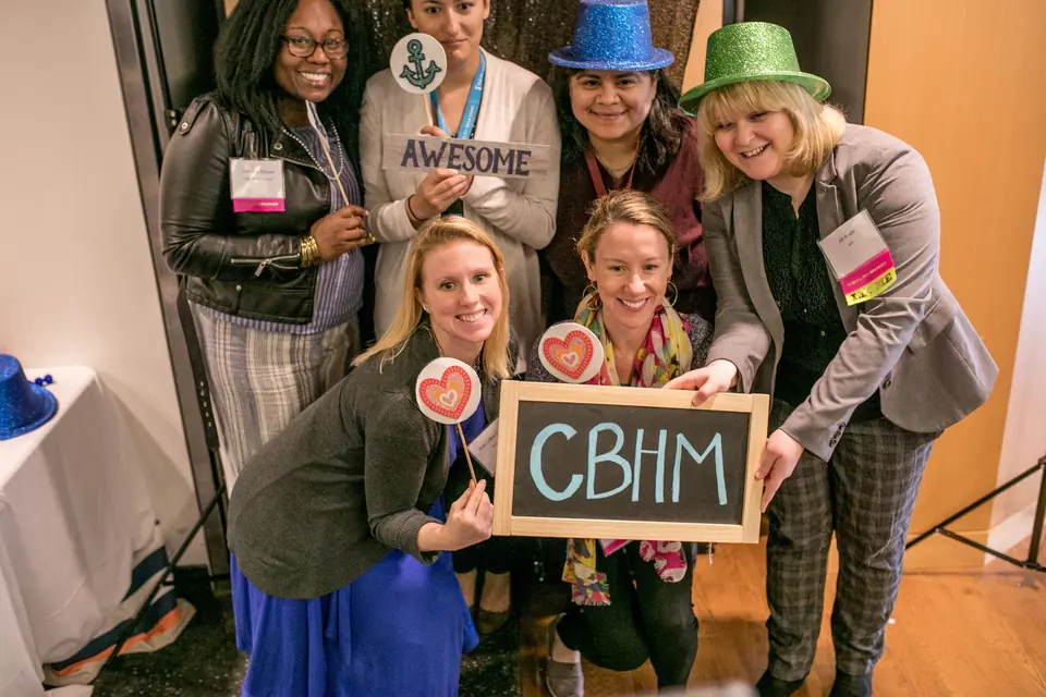 School psychologists celebrating together at the CBHM showcase, holding a sign that reads CBHM